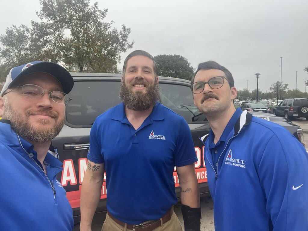 Three men are posing in front of a vehicle with a company logo for Houston Roofing. They are wearing blue branded shirts, proudly representing their team. Trees and a clear sky provide the perfect backdrop to showcase their commitment to quality service.