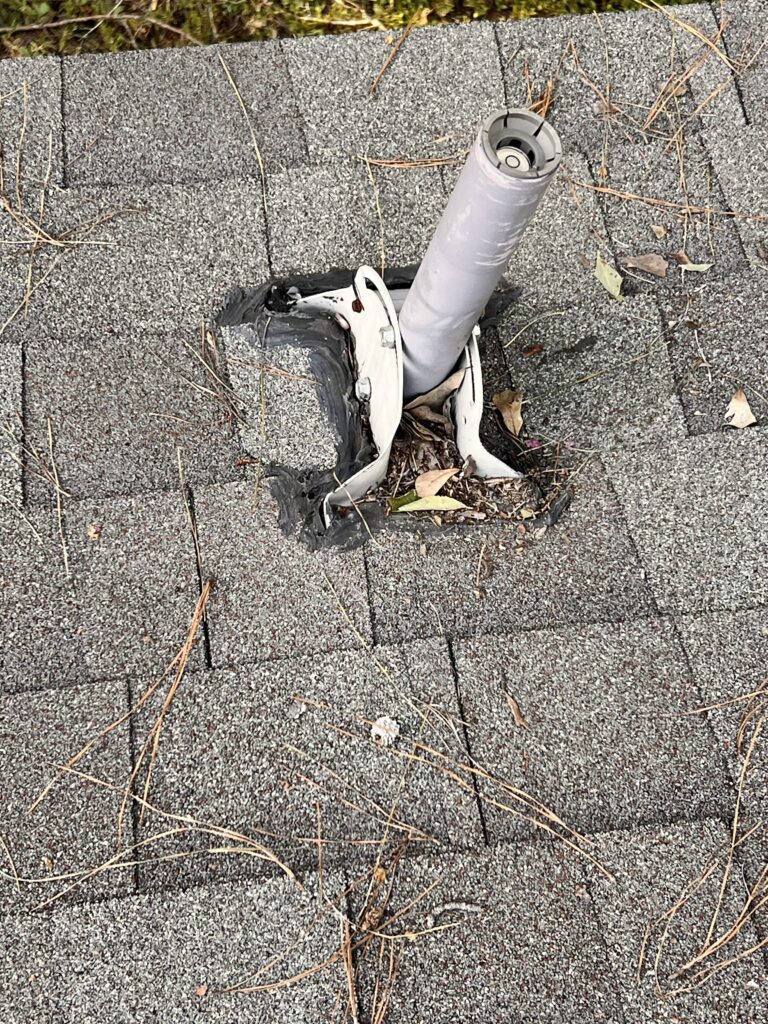 A damaged roof vent in Houston is surrounded by loose shingles and pine needles, with visible cracks and torn material around the base, suggesting a need for repair.