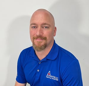 A man with a shaved head and a short beard, wearing a royal blue polo shirt with an