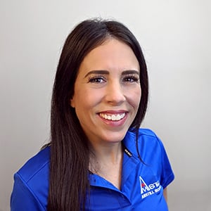 A woman with long dark hair smiles at the camera. She is wearing a blue polo shirt with a logo that appears to read