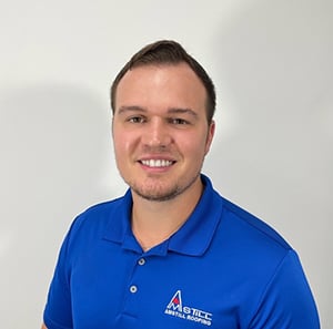 A man with short brown hair and a light beard is smiling at the camera, wearing a bright blue polo shirt with a company logo that reads