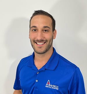 A smiling man with short dark hair, wearing a royal blue polo shirt emblazoned with a company logo that reads