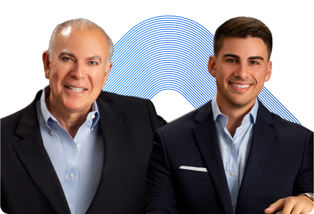 Two people are posed together and smiling against a background with a blue, wavy pattern. The person on the left has short, gray hair and wears a dark blazer over a light blue shirt. The person on the right has short, dark hair and wears a dark blazer over a light blue shirt.