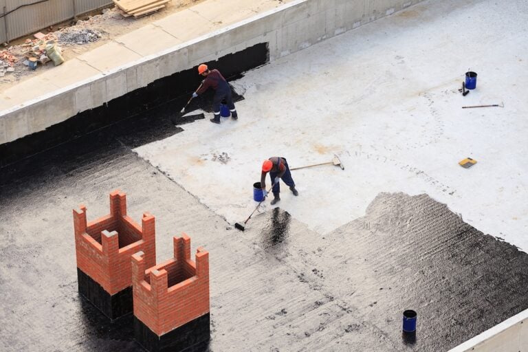 Two workers conduct waterproofing of flat roof with rollers.