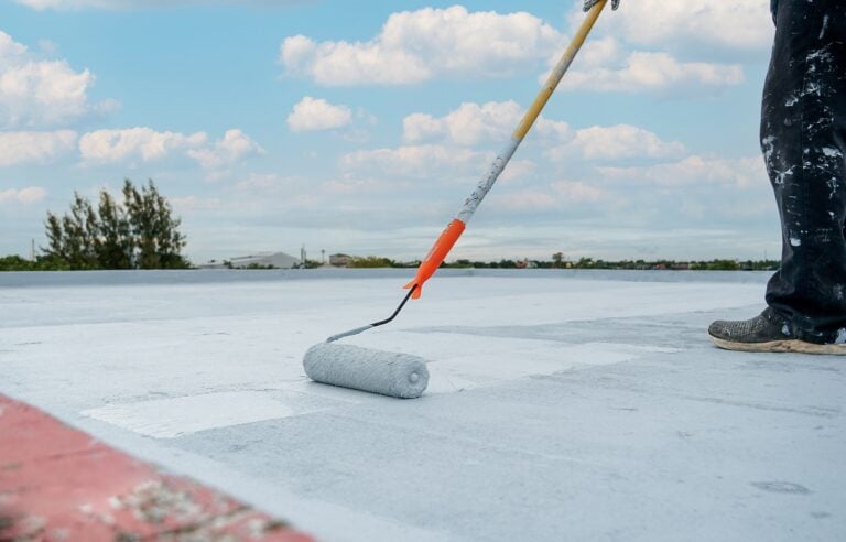paint rolling applying a white roof coating to a flat roof