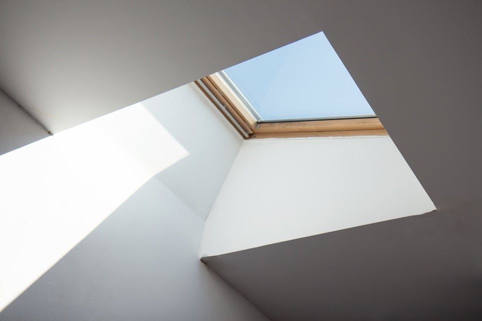Dormer wooden window in the white sloping ceiling. Square ceiling window. Looking up to the blue sky