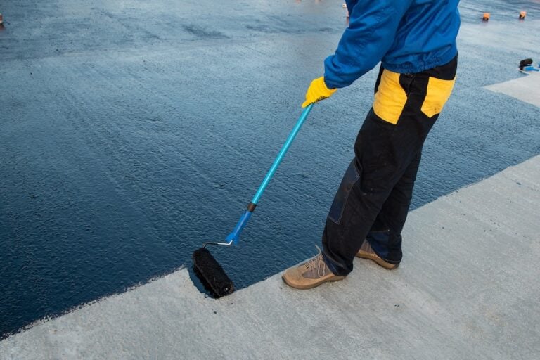 Black roof coating applied by a worker with a roller