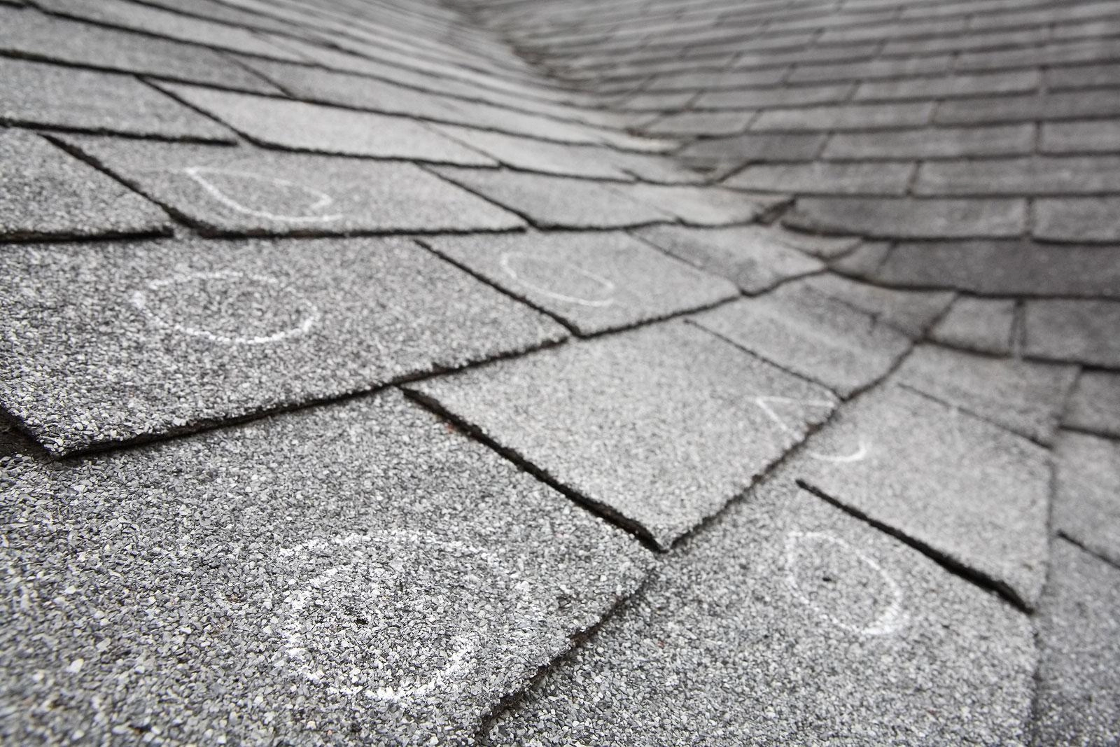 Close-up of a gray shingle roof with several chalk circles drawn on the shingles, indicating areas needing inspection or repair. The roof slopes away, giving perspective to the scene. Houston Roof Experts are ready to assess and address these potential issues.