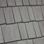 Close-up image of a section of a gray shingled roof, showing the texture and arrangement of the rectangular shingles in a neat, overlapping pattern.