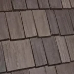 The image shows a close-up view of a roof covered with wooden shingles. The shingles are arranged in a staggered pattern, with each row overlapping the one below. The wood appears weathered, displaying various shades of brown.