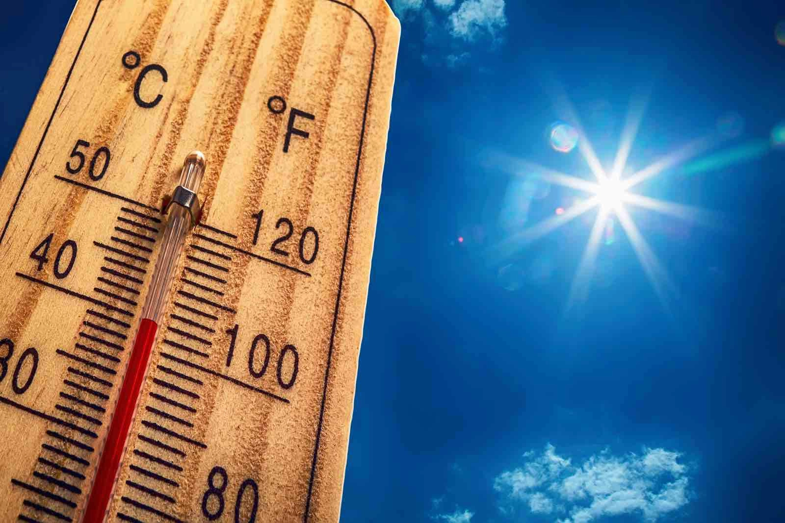 A wooden thermometer displays high temperatures in both Celsius and Fahrenheit under a bright sun and blue sky with a few clouds. The mercury level indicates a hot day, with the sun shining intensely in the background, reminding one of how Houston roof experts might weatherproof against such heat.