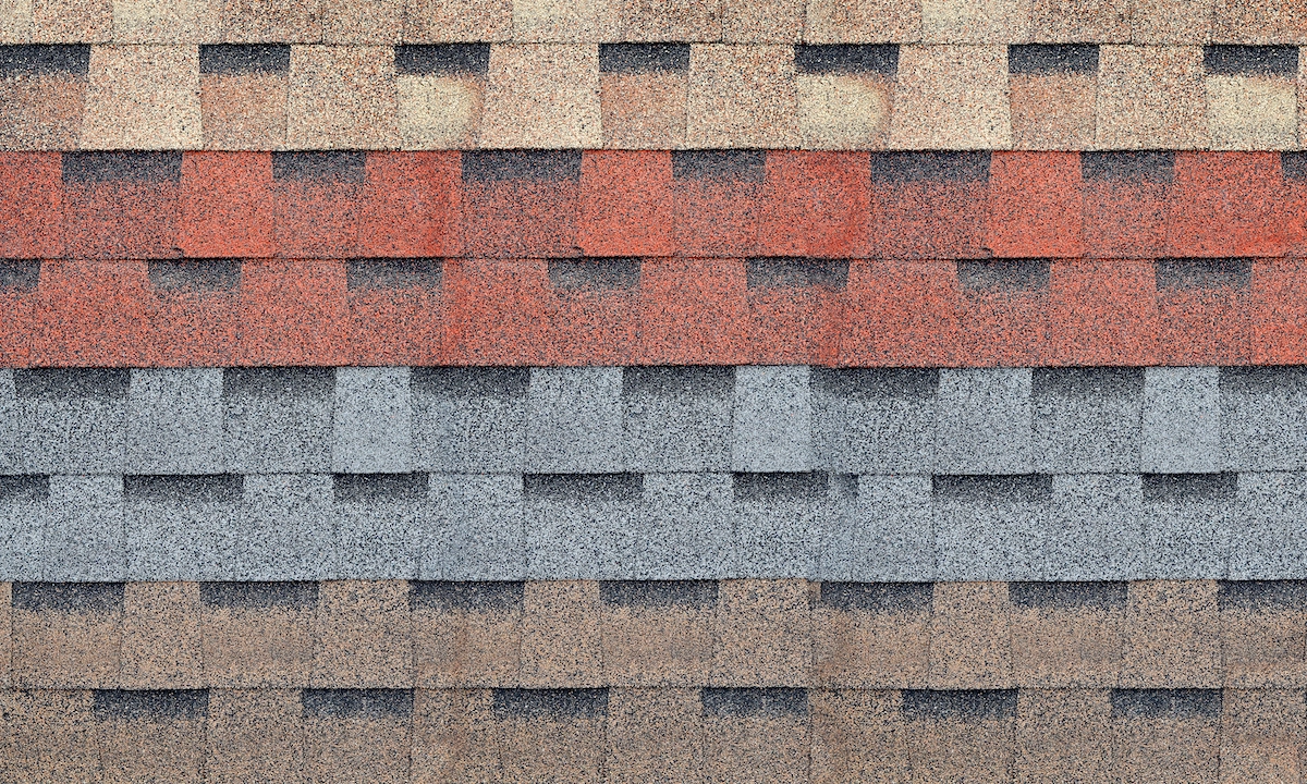Close-up of a wall featuring multiple rows of different colored roof shingles, as typically seen in Houston roofing. The shingles are organized in horizontal layers, each layer showcasing a distinct color: beige on top, followed by red, grey, brown, and dark brown at the bottom.