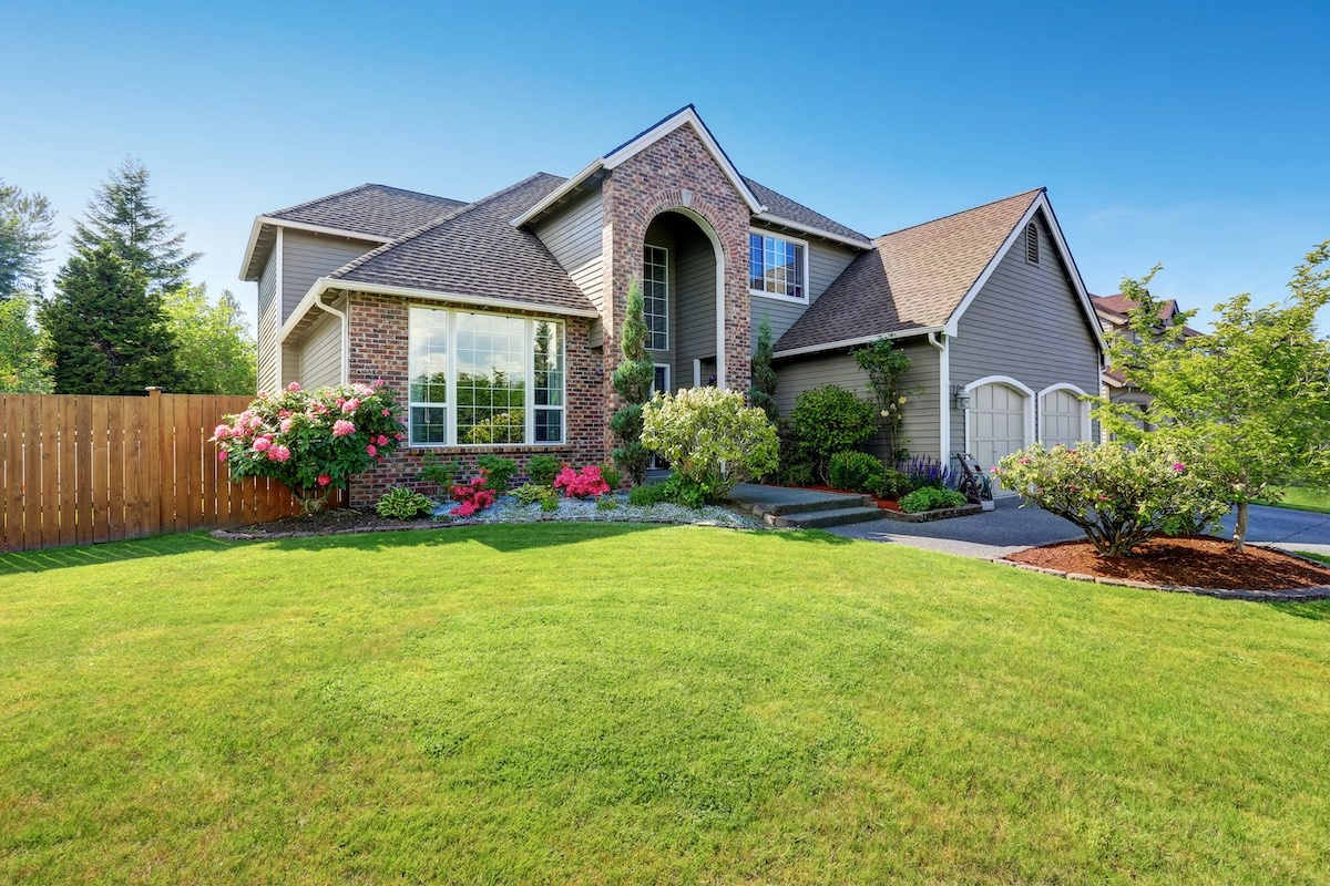 A beautiful suburban house with a mix of brick and siding exterior, large windows, and a well-maintained front yard. The lush green grass, blooming flowers, and shrubs create a picturesque scene under the clear blue sky. This charming home in Houston even features a recently completed roof replacement.