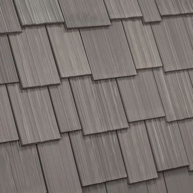 A close-up view of a roof with overlapping, rectangular, grey shingles. The shingles have a textured surface, arranged in a staggered pattern, giving the roof a layered appearance.