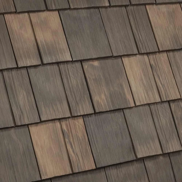 Image of a roof with wooden shingles. The shingles are arranged in a staggered pattern, displaying a variety of natural wood tones ranging from light to dark brown. The texture and grain of the wood are visible, giving a rustic appearance.
