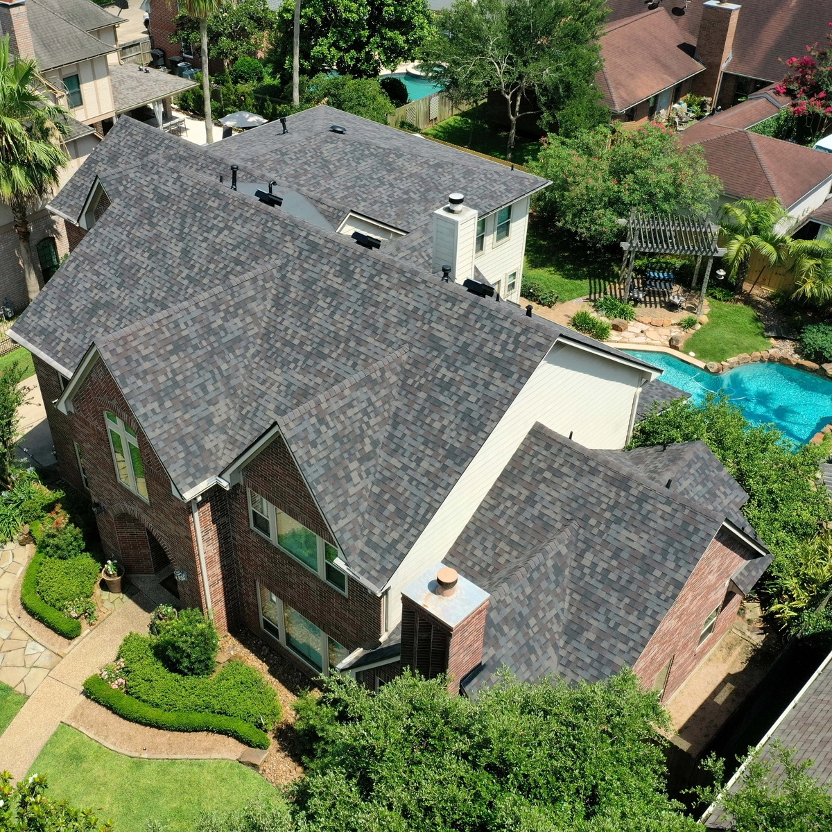overhead view of large shingle roof surrounded by trees with pool in background