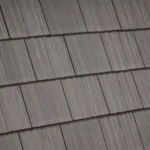 A close-up view of a grey shingle roof with neatly aligned rectangular shingles, showcasing their textured surfaces and overlapping pattern.