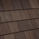 Close-up view of a roof with dark brown wooden shingles neatly arranged in a horizontal pattern. The shingles display natural wood texture and slight variations in color, adding depth and character to the roofing.