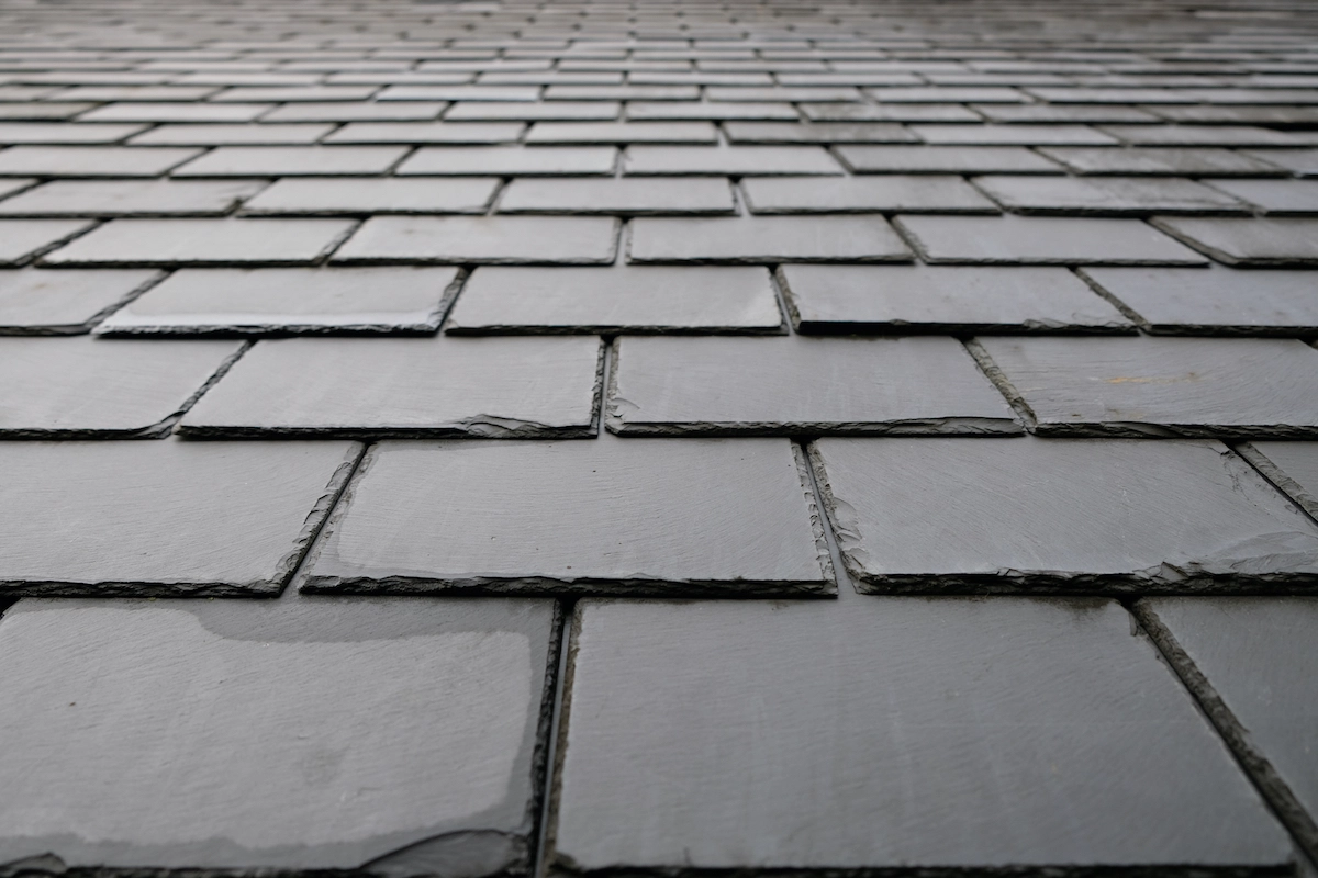 Close-up view of a slate roof, showing the arrangement of rectangular, overlapping slate tiles. The perspective is from the bottom, looking upwards, highlighting the uniform pattern and texture of the tiles with a slight sheen on the surface—an ideal reference for anyone considering a Houston roof replacement.