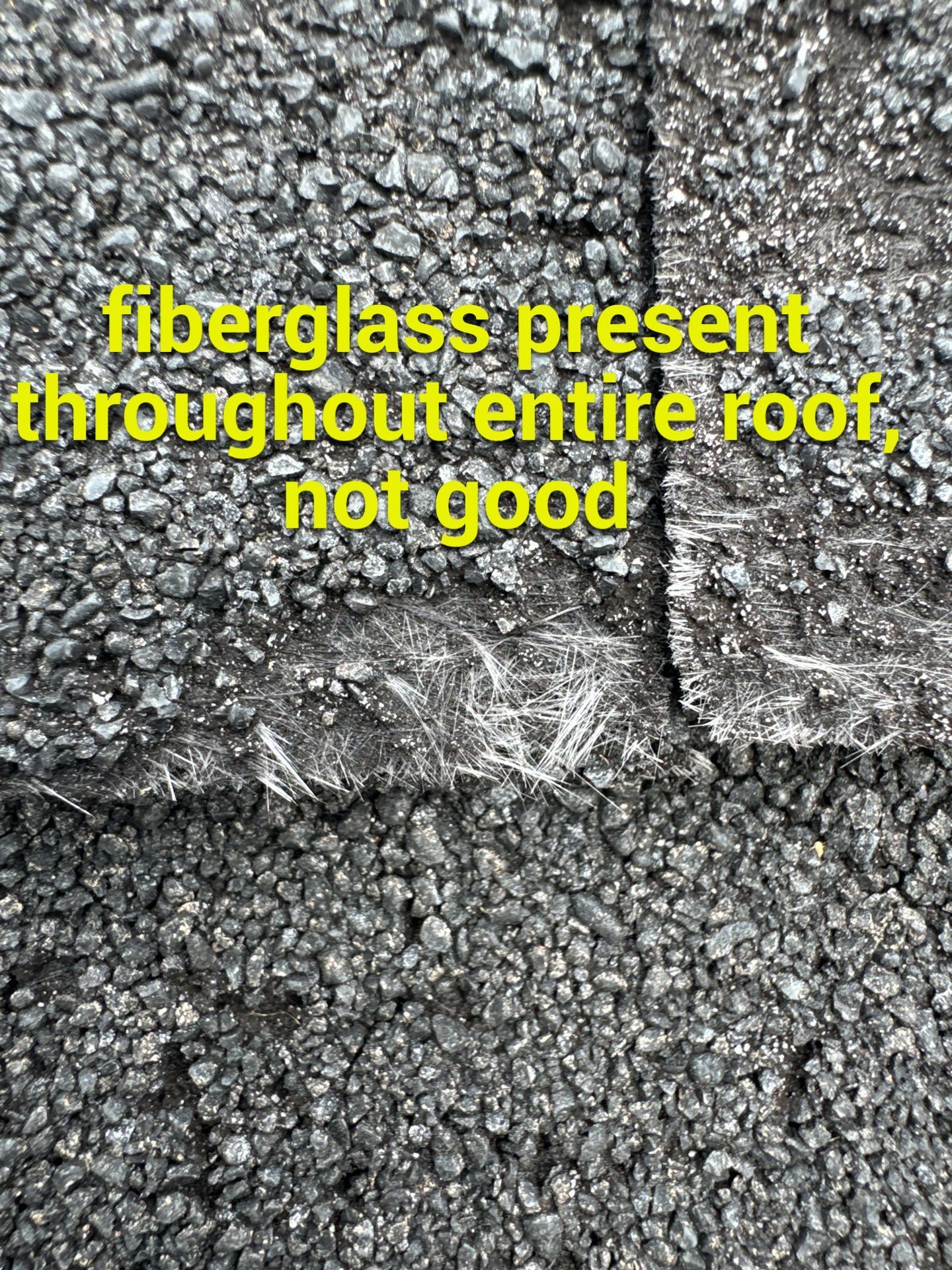 Close-up of a roof surface with exposed fiberglass fibers visible beneath shingles. Yellow text overlay reads, "fiberglass present throughout entire roof, not good.
